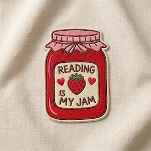 May include: Embroidered patch in the shape of a jam jar, with the text "READING IS MY JAM". The jar is red with a pink lid and a strawberry in the center. Two red hearts flank the strawberry.
