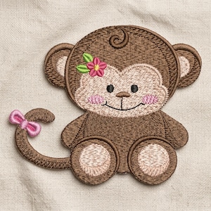 May include: An embroidered patch of a brown monkey with a light tan face, pink cheeks, and a small pink bow on its tail. The monkey features a small pink flower with green leaves tucked behind its ear, dark eyes, and a stitched smile.