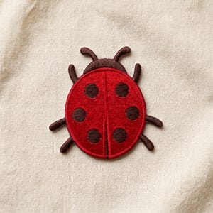 May include: Embroidered ladybug patch featuring a red body with six dark brown spots and brown antennae and legs. The patch is designed to be sewn or ironed onto fabric. The ladybug is a popular symbol of good luck and nature.