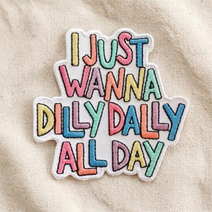 May include: Embroidered patch with the phrase "I JUST WANNA DILLY DALLY ALL DAY" in colorful, bubble-style letters. The patch has a white background and a black border, perfect for adding to clothing or accessories.