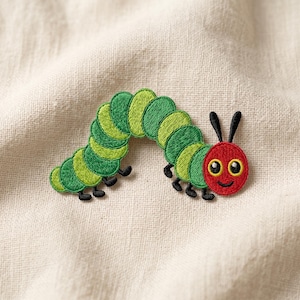 May include: Embroidered caterpillar patch featuring a red head with black antennae and a smiling face. The caterpillar's body is composed of green and light green segments. The patch is on a beige fabric background.