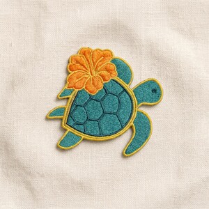 May include: An embroidered patch featuring a teal sea turtle with a dark teal shell and a bright orange hibiscus flower resting on its back. The turtle has a yellow border outline and is depicted in a flat, stylized design on a light fabric.