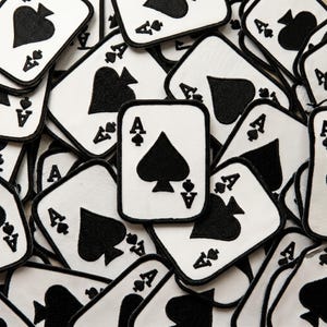 May include: A collection of rectangular embroidered patches featuring a white background with a black border. Each patch displays a black spade symbol in the center, with the letter A and a small spade icon in the top left and bottom right corners.