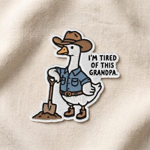 May include: Embroidered patch featuring a white goose wearing a brown cowboy hat, blue shirt, and brown boots, holding a shovel. Text reads "I'M TIRED OF THIS GRANDPA."