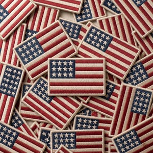May include: A collection of embroidered American flag patches. Each patch features a blue rectangle with white stars and red and white stripes, with a cream-colored border. The patches are scattered across the image.
