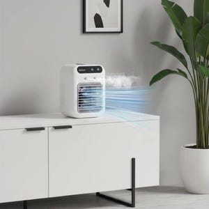 May include: A white portable air cooler with a rectangular body, a front grille, and a black control panel on top. The device emits a visible mist and blue light streaks from the front vents, indicating airflow, while resting on a white cabinet.