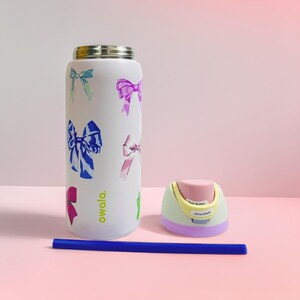 May include: White water bottle with colourful bow designs, a matching lid, and a blue straw. The lid has a push button and the text "Lift to Unlock". The bottle is approximately 25 cm tall.
