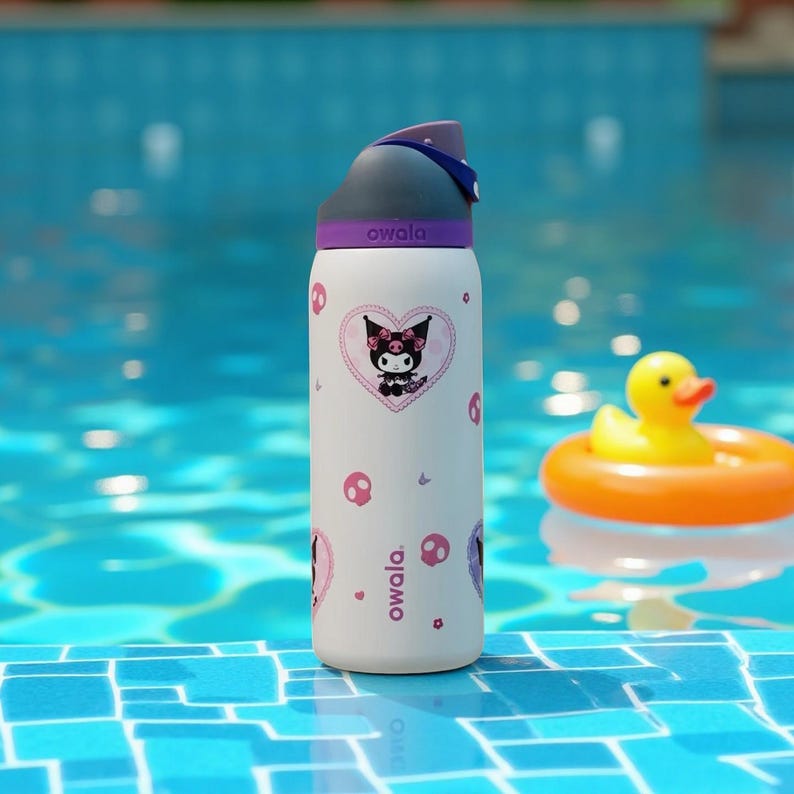 May include: White Owala water bottle featuring a cartoon character design in black and pink. The bottle has a grey lid with a purple accent and a blue strap. The bottle is decorated with heart-shaped graphics, cartoon characters, and skull designs. A yellow rubber duck in an orange float is in the background.