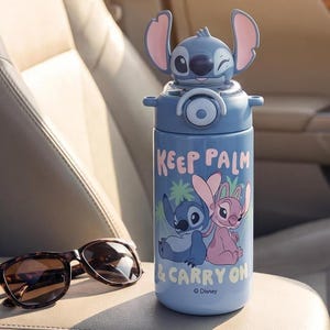 Op de afbeelding: Een blauwe waterfles met een Stitch-personageontwerp op het deksel. De fles heeft de tekst "KEEP PALM & CARRY ON" en een afbeelding van Stitch en Angel. Een zonnebril met schildpadmotief ligt ernaast.