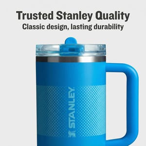 May include: A blue Stanley mug with a handle and a clear lid. The mug has the Stanley logo and the text "Trusted Stanley Quality" and "Classic design, lasting durability".