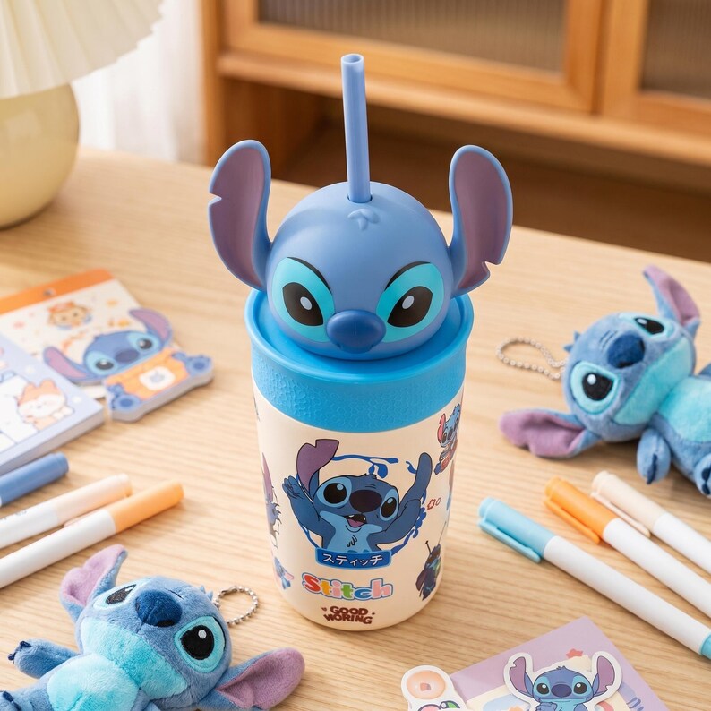 May include: A blue and white Stitch-themed tumbler with a straw, featuring a 3D character head on top. The tumbler has a cartoon graphic of Stitch and the text "Good Morning". Other Stitch-themed items, including a plush toy and notepads, are also visible.