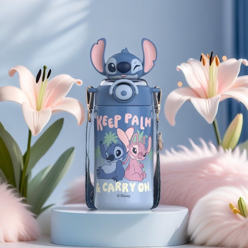 Op de afbeelding: Een blauwe waterfles met een cartoonkarakterontwerp en de tekst "KEEP PALM & CARRY ON". De fles heeft een riem en een karakterkop erop. De achtergrond bevat roze bloemen en een witte sokkel.