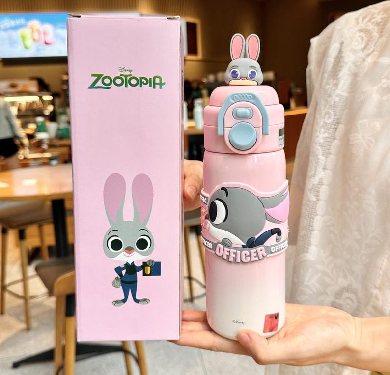以下が含まれることがあります： ピンク色のズートピアをテーマにしたウォーターボトル。漫画のウサギのデザイン。ボトルは水色の蓋と、ズートピアのロゴとキャラクターのイラストが描かれたお揃いの箱が付いています。ボトルはピンクから白へのグラデーションでデザインされています。