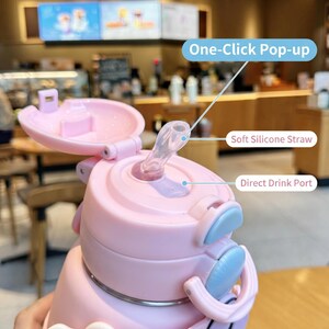 May include: Pink water bottle with a flip-top lid and a soft silicone straw. Features a one-click pop-up mechanism and a direct drink port. The bottle has light blue accents and is designed for easy use.