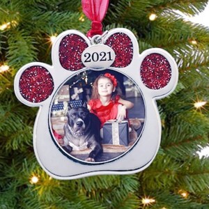 Pu&ograve; includere: Un ornamento a forma di impronta di zampa argentata con accenti di glitter rosso. L'ornamento ha un inserto fotografico trasparente con una foto di una ragazza e un cane. L'ornamento ha anche un'etichetta argentata con l'anno 2021.