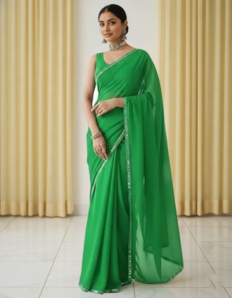 Puede incluir: Un sari verde esmeralda sin mangas con un borde brillante. La tela se drapea elegantemente, creando pliegues suaves. El sari es una prenda tradicional, a menudo usada para ocasiones especiales.