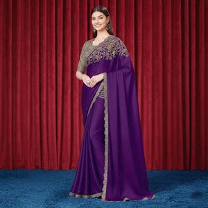 May include: A deep purple saree featuring a smooth, satin-like finish and a contrasting light-coloured embroidered border. The garment includes a matching short-sleeved blouse with intricate floral embroidery across the shoulders and chest area.