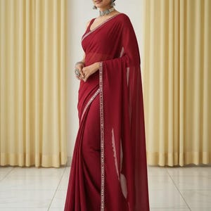 Puede incluir: Un sari burdeos con un borde adornado con plata y un ribete a juego. La elegante prenda presenta un dise&ntilde;o sin mangas y est&aacute; elegantemente drapeada. El sari se combina con joyas de plata, creando un conjunto sofisticado.