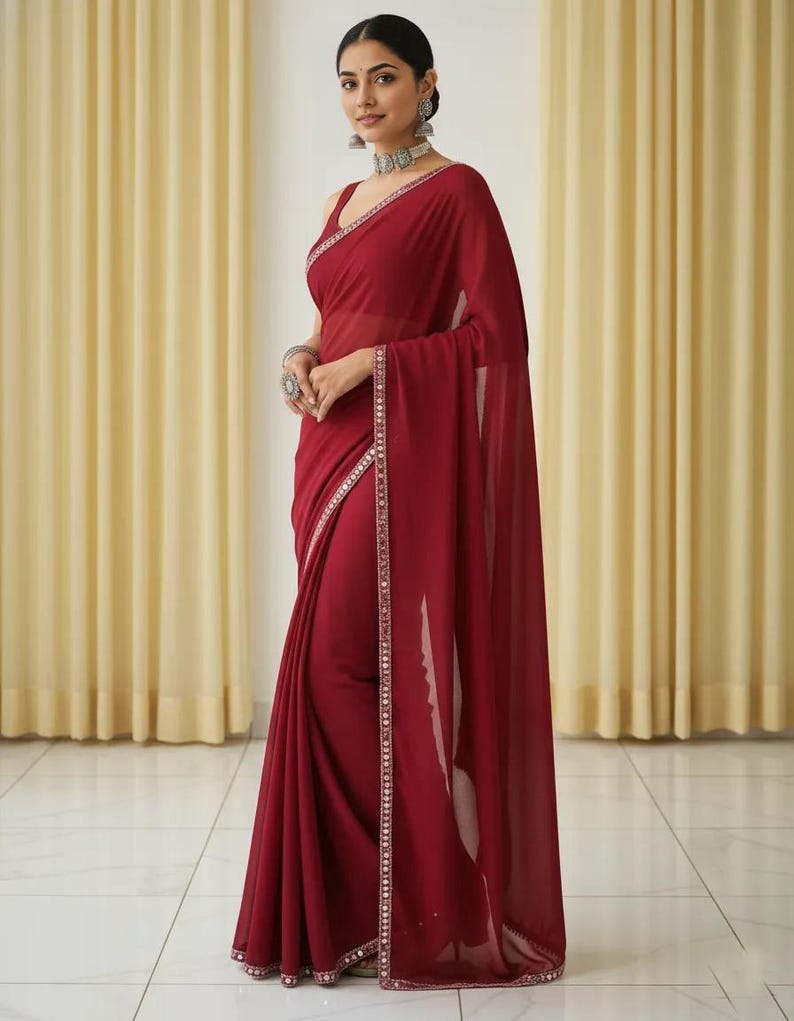 Puede incluir: Un sari burdeos con un borde adornado con plata y un ribete a juego. La elegante prenda presenta un dise&ntilde;o sin mangas y est&aacute; elegantemente drapeada. El sari se combina con joyas de plata, creando un conjunto sofisticado.