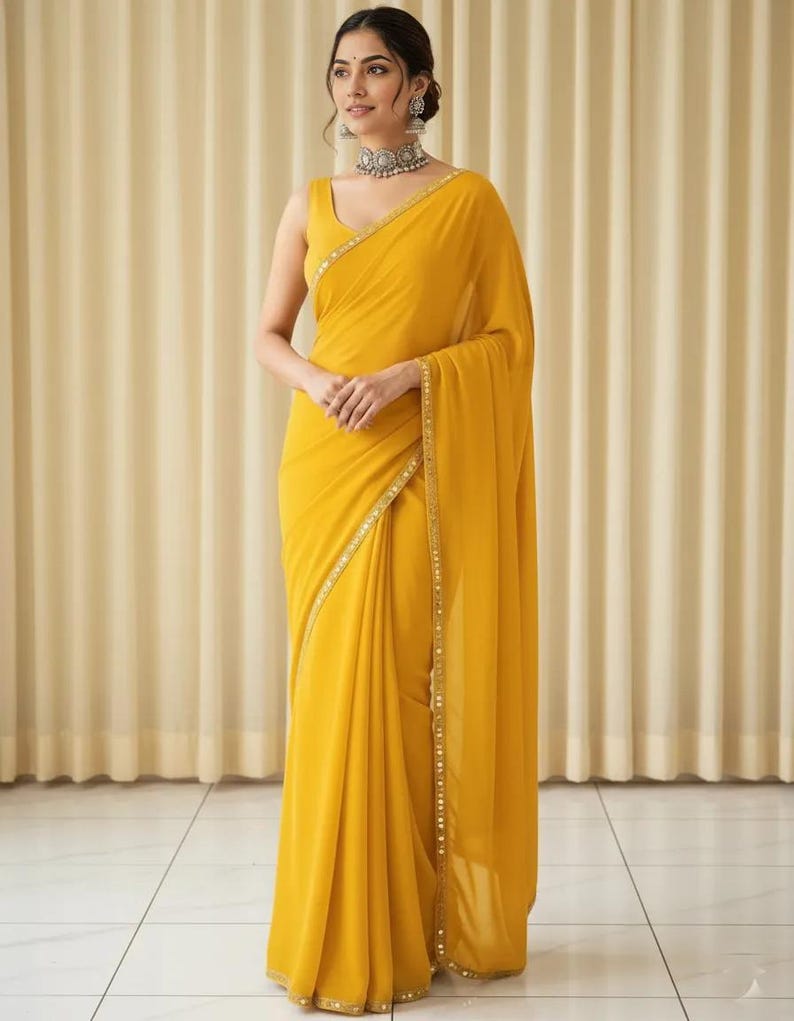 Puede incluir: Un sari amarillo vibrante con una blusa sin mangas. El sari presenta un delicado borde dorado y est&aacute; elegantemente drapeado. La mujer lleva joyas de plata, incluyendo un collar y pendientes. El fondo es beige neutro.