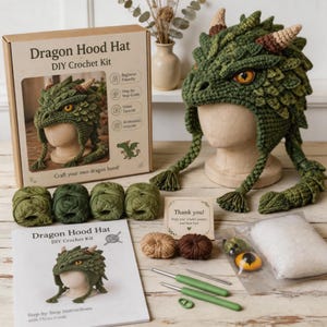Puede incluir: Un kit de ganchillo DIY Dragon Hood Hat que incluye una caja de cartón con texto, un gorro de dragón verde terminado sobre una cabeza de maniquí, cuatro ovillos de lana verde, dos ovillos marrones pequeños, un manual de instrucciones y relleno.