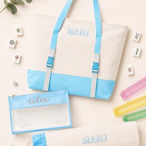 Può includere: Una borsa tote color crema e azzurro con la scritta MAHJ, una sacca cilindrica con coulisse abbinata con la scritta MAHJ e una pochette rettangolare trasparente con la scritta tiles. Il set include tessere del mahjong, dadi e rastrelliere colorate.