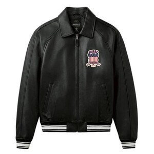 May include: Black leather jacket with a zip-up front, collar, and a patch on the chest. The jacket has white and black striped cuffs and hem. The patch features a design with the American flag and the word "AVIREX".