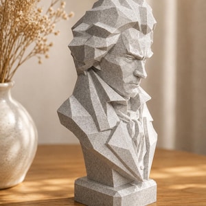 Könnte beinhalten: Eine hellgraue, gesprenkelte, geometrische Büste einer Person mit strengem Gesichtsausdruck, die durch scharfe, kantige Facetten an Haar, Gesicht und Kleidung besticht und auf einem rechteckigen Sockel mit steinartiger Textur steht.