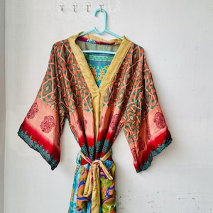 May include: A long-sleeved kimono robe featuring a vibrant mix of orange, red, teal, and gold patterns. The garment has a solid gold-coloured collar and a matching tie belt at the waist, with wide sleeves and a repeating paisley and geometric print.
