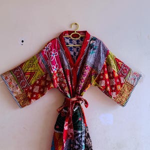 May include: A long-sleeved robe featuring a patchwork design with various colorful fabric patterns including red, yellow, green, and purple. The garment has a V-neckline, wide sleeves, and a matching fabric tie belt at the waist.