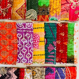 Puede incluir: Una colección de piezas de tela coloridas y estampadas, probablemente textiles o colchas. Las telas muestran una variedad de diseños, incluyendo patrones florales, geométricos y abstractos, en tonos de rojo, naranja, amarillo, verde, morado y rosa. Cada pieza está cosida con hilo blanco.