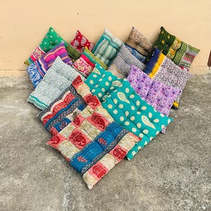 May include: A collection of square floor cushions featuring various colorful patterns, including paisley, floral, and geometric designs. Each cushion is quilted with visible stitching and displays a mix of vibrant colors like red, blue, green, and purple.