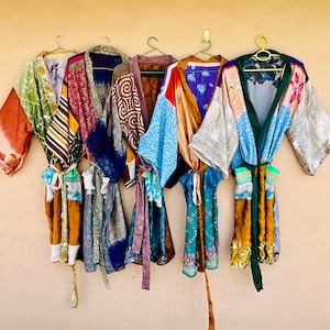 May include: A collection of colorful, patterned silk robes hanging on a wall. The robes feature a variety of designs, including floral, geometric, and abstract patterns. Each robe has a unique color palette, with hues of blue, green, orange, and pink.