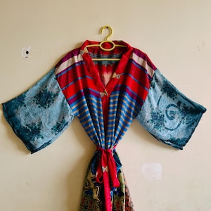 May include: A kimono-style robe featuring a vibrant mix of patterns and colors. The upper section displays red and blue vertical stripes, while the wide sleeves showcase a light blue floral print. A matching fabric tie belt cinches the waist.