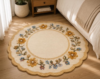 May include: A round, cream-colored area rug with a scalloped edge and a border featuring a raised, tufted floral vine pattern. The design includes yellow and blue flowers with green leaves arranged in a circular motif on a solid center.
