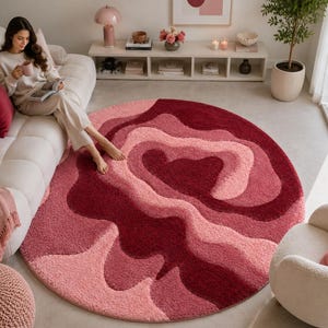 May include: A large, circular area rug featuring a textured, shaggy pile with an abstract, layered design in varying shades of deep burgundy, vibrant red, and soft pastel pink, creating a fluid, organic pattern across the entire surface.
