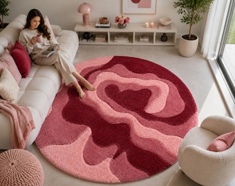 May include: A large, circular area rug featuring a textured, shaggy pile with an abstract, layered design in varying shades of deep burgundy, vibrant red, and soft pastel pink, creating a fluid, organic pattern across the entire surface.