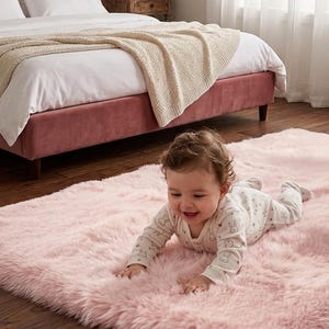 May include: A rectangular, light pink faux fur area rug with a long, soft pile texture. The rug is positioned on a dark wood floor, providing a plush surface. The material appears thick and shaggy, covering a significant portion of the floor area.