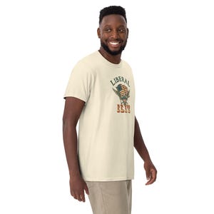 May include: Cream-colored t-shirt with a graphic that reads "LIBERAL ELITE." The graphic features an American flag design with a skull. The shirt is made of a soft material and has short sleeves.