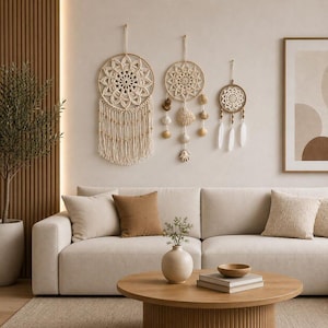 May include: Three circular wall hangings featuring intricate cream-colored macrame patterns. The largest has long fringe and wooden beads, the middle one includes hanging seashells, and the smallest features white feathers and wooden beads.