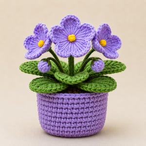 Könnte beinhalten: Eine gehäkelte Veilchenpflanze in einem lila Topf. Die Pflanze hat drei große, hellviolette Blüten mit gelben Zentren, grüne Blätter und ungeöffnete Knospen. Der Topf hat einen passenden Lilaton.