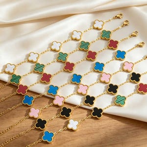 Peut inclure: Une collection de bracelets à chaîne dorée ornés de multiples breloques en forme de trèfle à quatre feuilles. Les breloques sont incrustées de matériaux de diverses couleurs, dont blanc, vert rayé, rouge, bleu, rose et noir, avec fermoir.