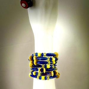Puede incluir: Un conjunto de pulseras de cuentas azules y amarillas de diferentes formas y tama&ntilde;os. Las pulseras est&aacute;n en un brazo de maniqu&iacute; blanco.