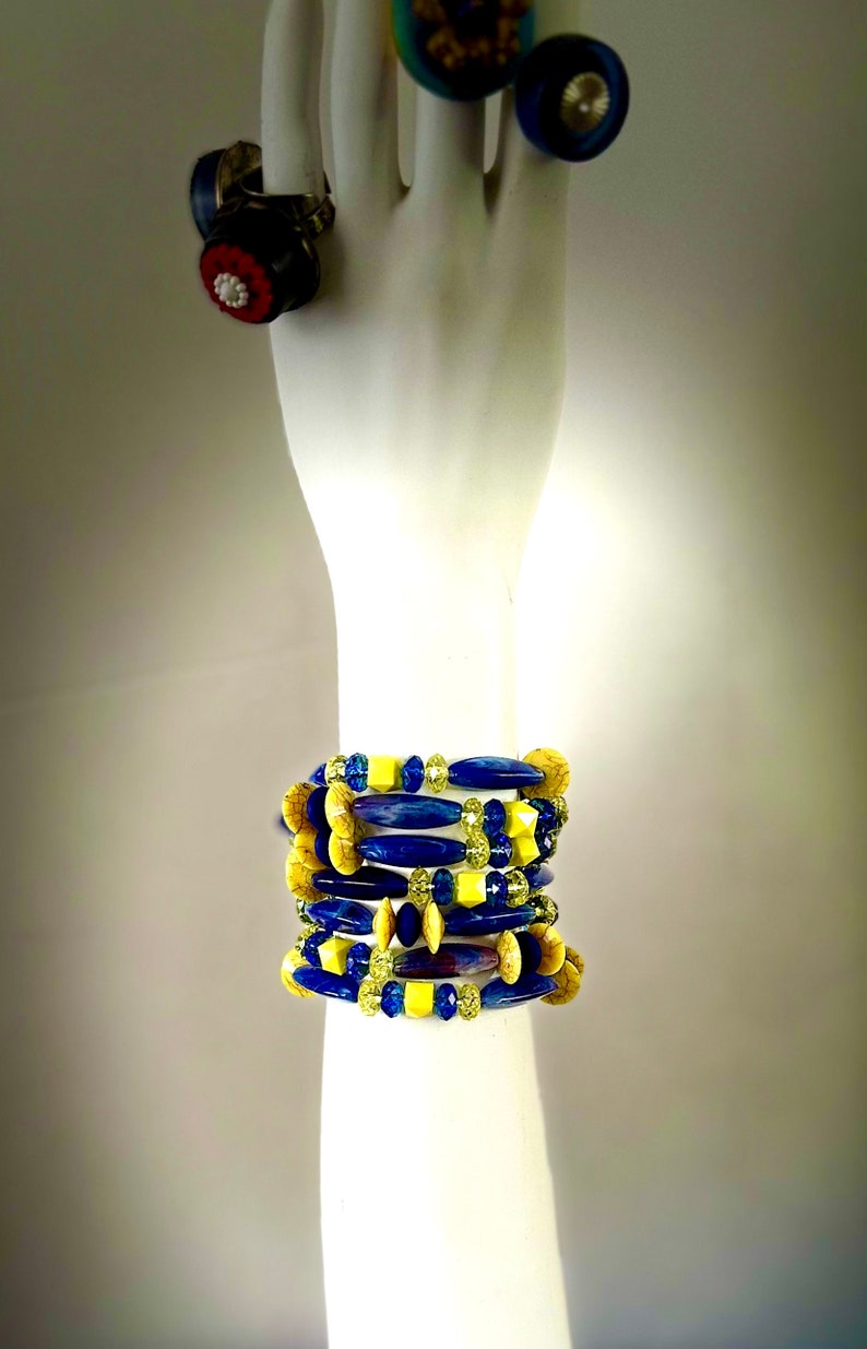 Puede incluir: Un conjunto de pulseras de cuentas azules y amarillas de diferentes formas y tama&ntilde;os. Las pulseras est&aacute;n en un brazo de maniqu&iacute; blanco.