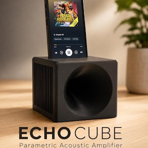 Op de afbeelding: Een zwarte kubusvormige passieve akoestische versterker met het label ECHOCUBE Parametric Acoustic Amplifier. Het apparaat heeft een grote ronde opening aan de voorzijde en zijlamellen, met een smartphone in de bovenste gleuf geplaatst.