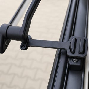 Könnte beinhalten: Ein matt-schwarzer Fensterverriegelungsmechanismus aus Metall mit einem Scharnierarm und einer Halterung. Die Baugruppe umfasst eine Montagebasis mit einer sichtbaren Schraube, einen horizontalen Auslegerarm und ein rechteckiges Schließblech mit Schraube.