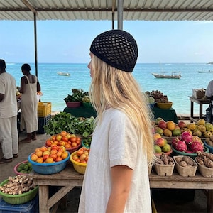 May include: A black crochet beanie with a wide-knit, open-weave pattern. The hat features a rounded crown and a solid, tight-knit border around the edge, providing a textured, lightweight appearance suitable for casual wear.