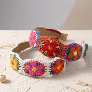 May include: Two colorful crochet headbands. One is white with yellow, pink, and orange floral designs. The other is orange with red, pink, and white floral designs. Both have a brown interior.