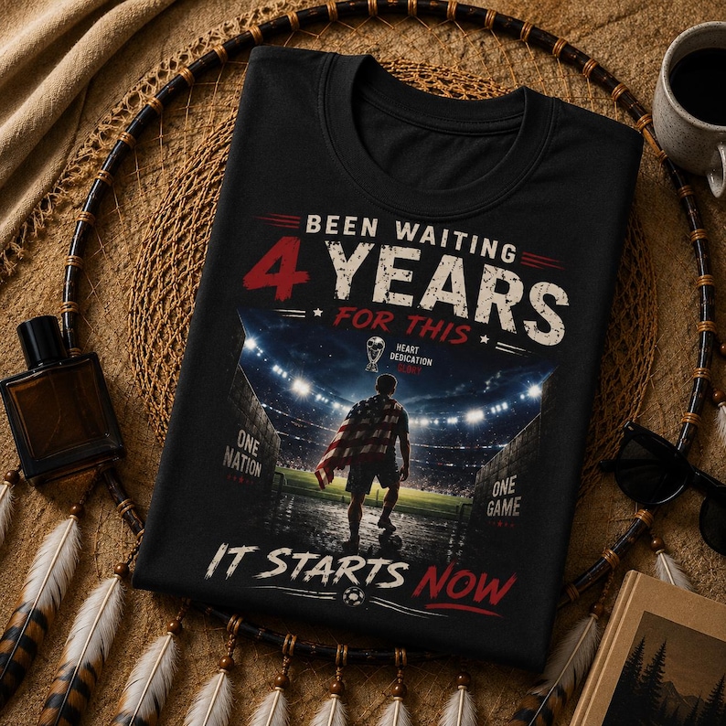 May include: Black t-shirt with the text "Been Waiting 4 Years For This". The shirt features a graphic of a person on a soccer field with a flag, and the words "One Nation, One Game, It Starts Now".