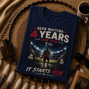 May include: Navy blue t-shirt with the text "Been Waiting 4 Years For This" in red and white. The shirt features a graphic of a soccer player in a stadium with the text "World Cup 2026" and "It Starts Now".